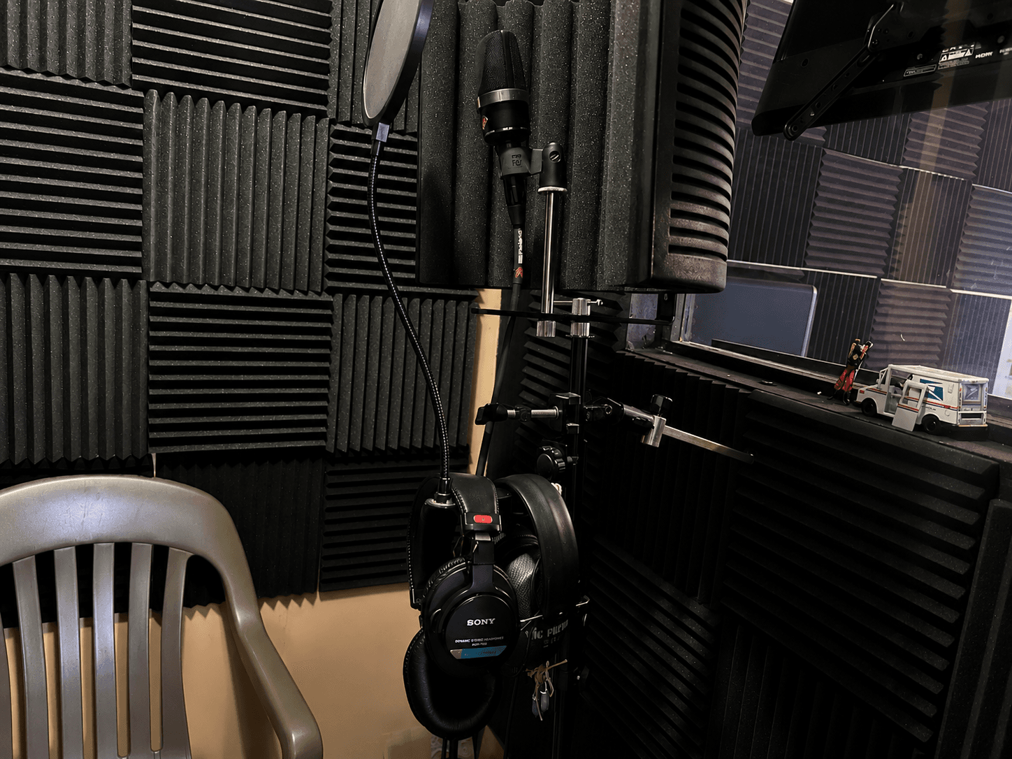 Recording studio setup with a microphone, pop filter, and headphones against black acoustic foam walls.
