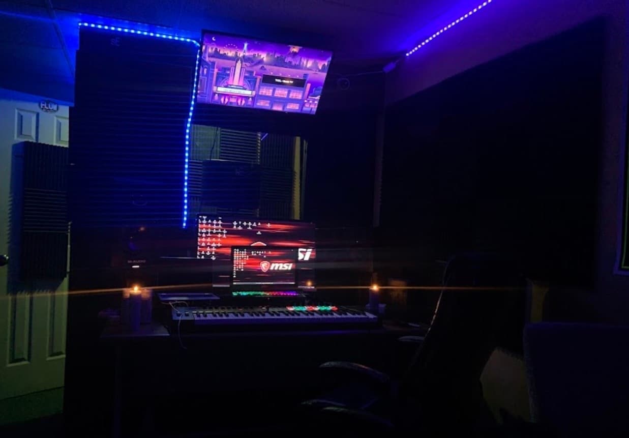 Dark music studio with blue LED lighting, multiple monitors, a MIDI keyboard, and lit candles.